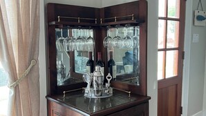 A bar area with a wooden counter, wine glasses, bottles, and a decorative bird hanging on the wall. - Anchors Aweigh (Cape Charles)