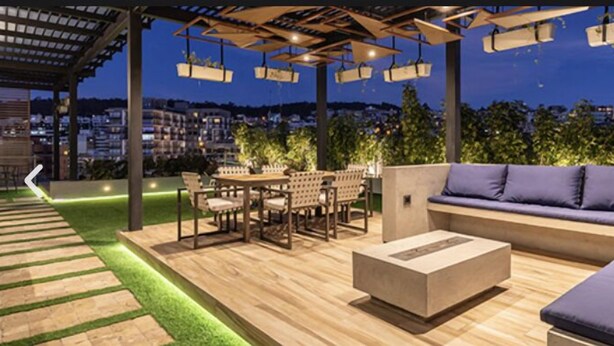 An outdoor patio with a wooden deck, a round table with chairs, a sofa, and hanging planters. - Modern apartment in Quito (Quito)
