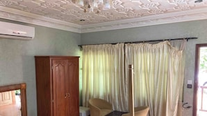 Una habitació amb un llit, un armari de fusta, dues cadires, una taula petita i una cortina.