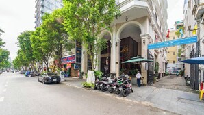 A street with parked motorcycles, a building with a sign, and a few people.