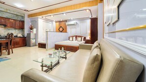 A modern hotel room with a glass coffee table, a sofa, a bed, and a kitchen area.
