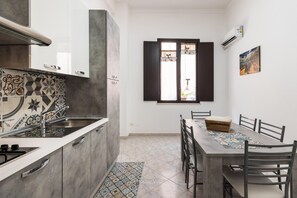 Eine kleine Küche mit gefliestem Spritzschutz, ein Essbereich mit Tisch und Stühlen sowie ein Fenster mit Vorhängen.