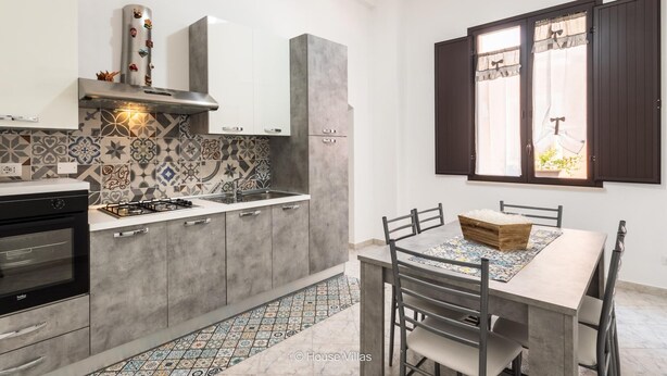 Une cuisine moderne avec des meubles gris, un pare-feu décoré et un coin repas comprenant une table et des chaises.