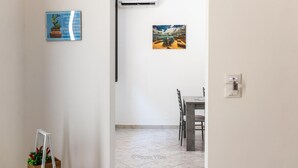 Un couloir mène à une salle à manger où se trouvent une table et des chaises, un appareil de climatisation et un tableau encadré accroché au mur.