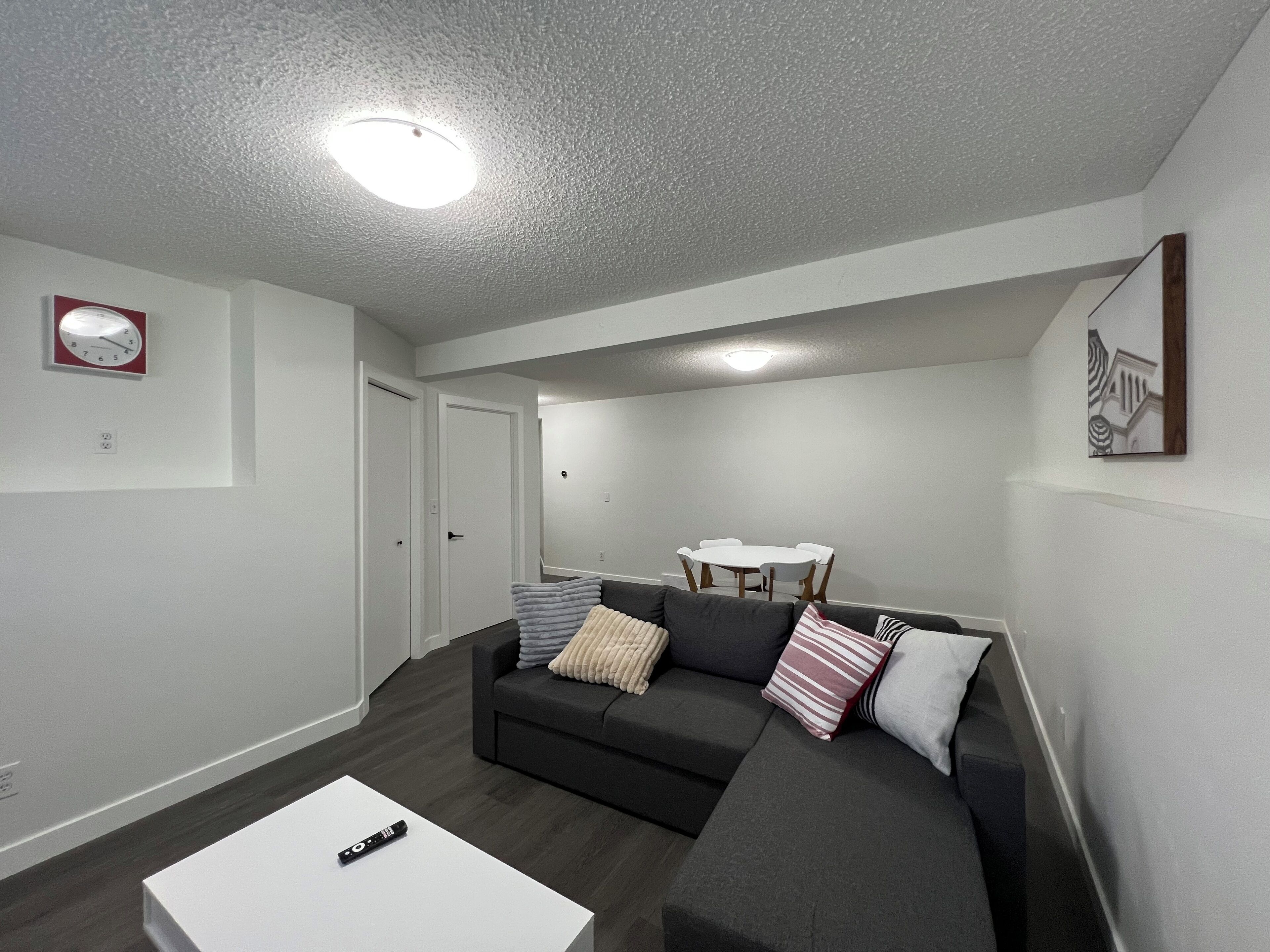 A modern living room with a dark grey sofa, a white coffee table, and a dining area with a white table and chairs.