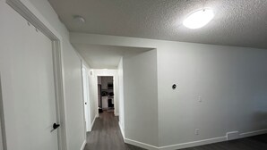 A hallway with white walls and dark wooden flooring, leading to a kitchen area with cabinets and appliances. - Cozy  3 beds Suite Near Calgary Airport, Quiet, Clean & Convenient Sleeps 7 (Calgary)
