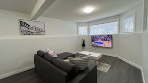 A modern living room with a gray sofa, a flat-screen TV, and a painting on the wall. - Cozy  3 beds Suite Near Calgary Airport, Quiet, Clean & Convenient Sleeps 7 (Calgary)