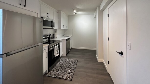 A modern kitchen with white cabinets, stainless steel appliances, and a patterned rug. - Cozy  3 beds Suite Near Calgary Airport, Quiet, Clean & Convenient Sleeps 7 (Calgary)