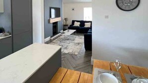 Una cocina moderna con una isla central, vigas de madera y una zona de comedor con una mesa lista para dos.