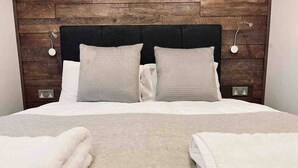 Una cama bien hecha con dos almohadas y dos toallas dobladas sobre un piso alfombrado.