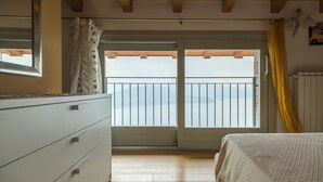 Ein Schlafzimmer mit Holzbalkendecke, einem großen Fenster mit Meerblick, einem Bett und einer Kommode.