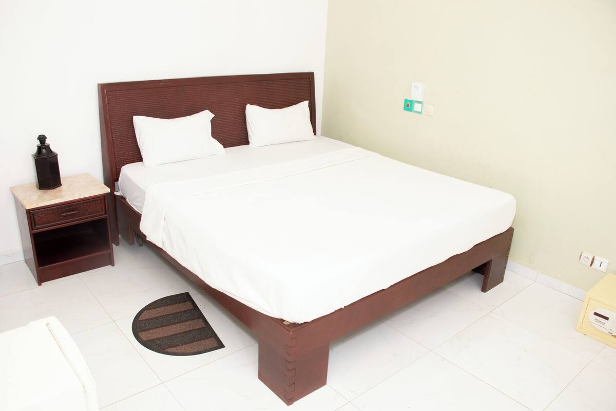 A neatly made bed with white linens, a wooden headboard, and a small bedside table with a lamp.