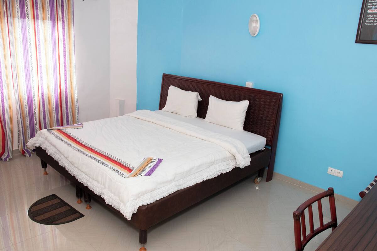 A bedroom with a bed, a chair, a curtain, and a wall socket.
