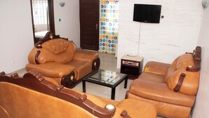A living room with two brown leather sofas, a glass coffee table, and a television mounted on the wall. - Alafia Hotel Ketou (Kétou)