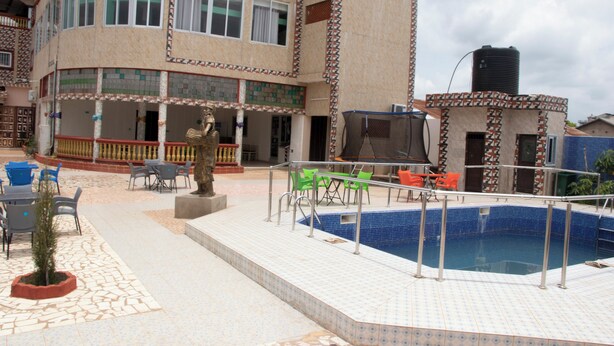 An outdoor swimming pool area with a tiled deck, a statue, and outdoor seating. - Alafia Hotel Ketou (Kétou)