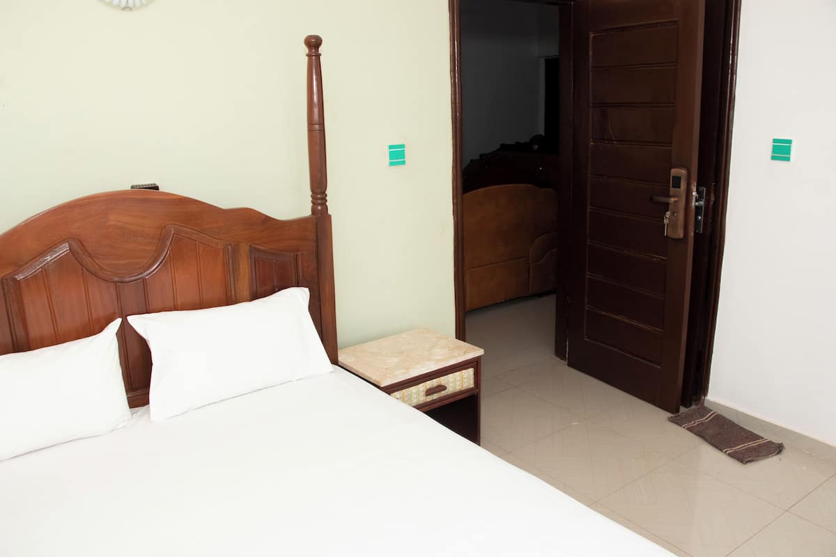 A hotel room with a wooden bed, a small bedside table, and a door leading to another room.