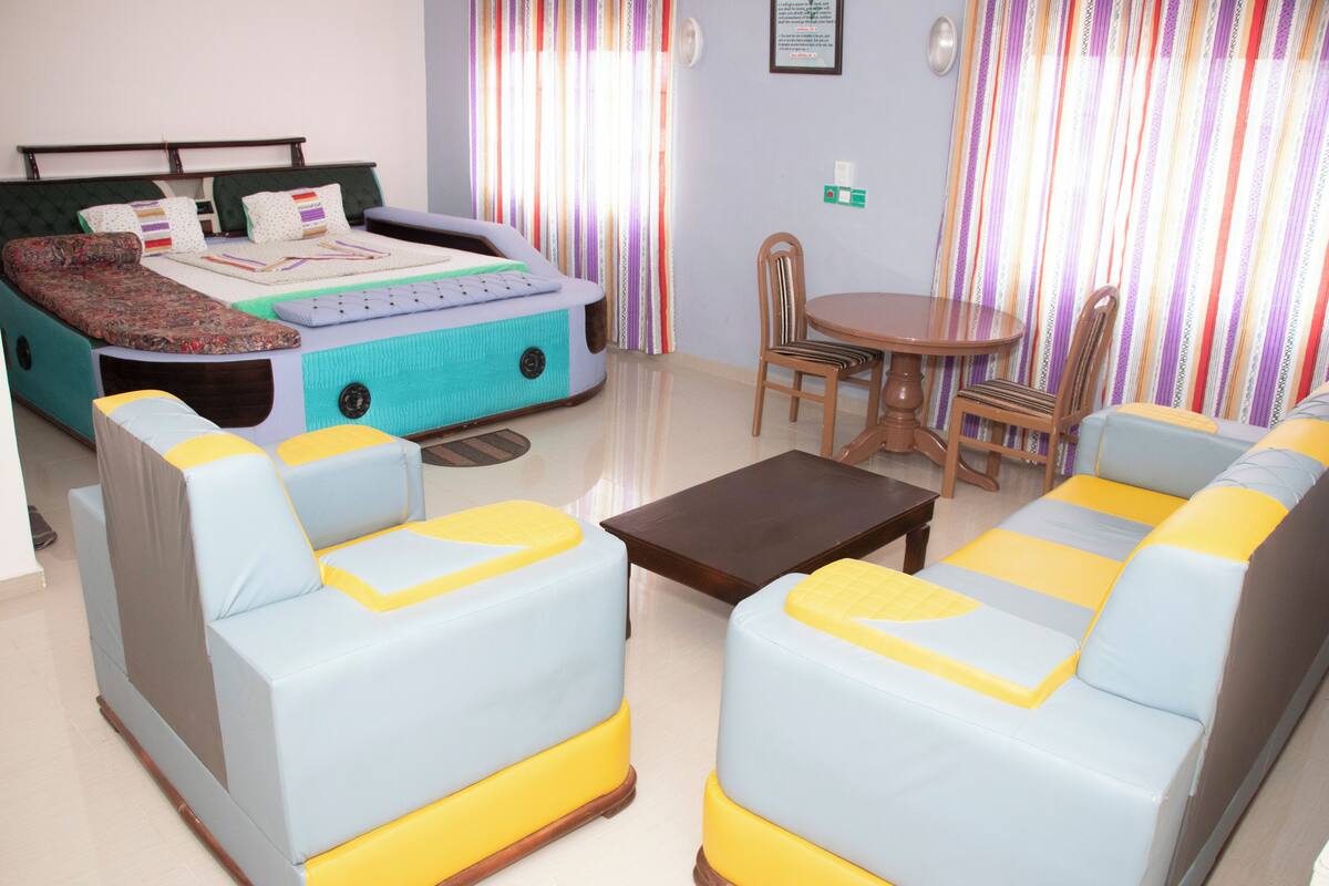 A room with a bed, two sofas, a small table, and curtains.