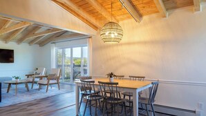 Une pièce spacieuse avec un plafond en bois, une table à manger avec des chaises, une grande fenêtre et un luminaire suspendu.