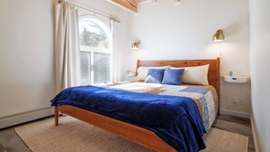 Une chambre avec un lit en bois, une grande fenêtre avec des rideaux et deux lampes de chevet.