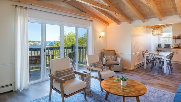 Un vaste espace de vie avec balcon, des poutres apparentes en bois au plafond et un coin repas donnant sur une cuisine située à l’arrière.