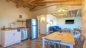 Une cuisine moderne dotée d’un réfrigérateur en acier inoxydable, de poutres en bois au plafond et d’un coin repas avec une table et des chaises en bois.