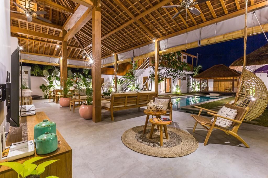 Espaço de convivência interno e externo com piscina, mobiliário de madeira e plantas em vasos.