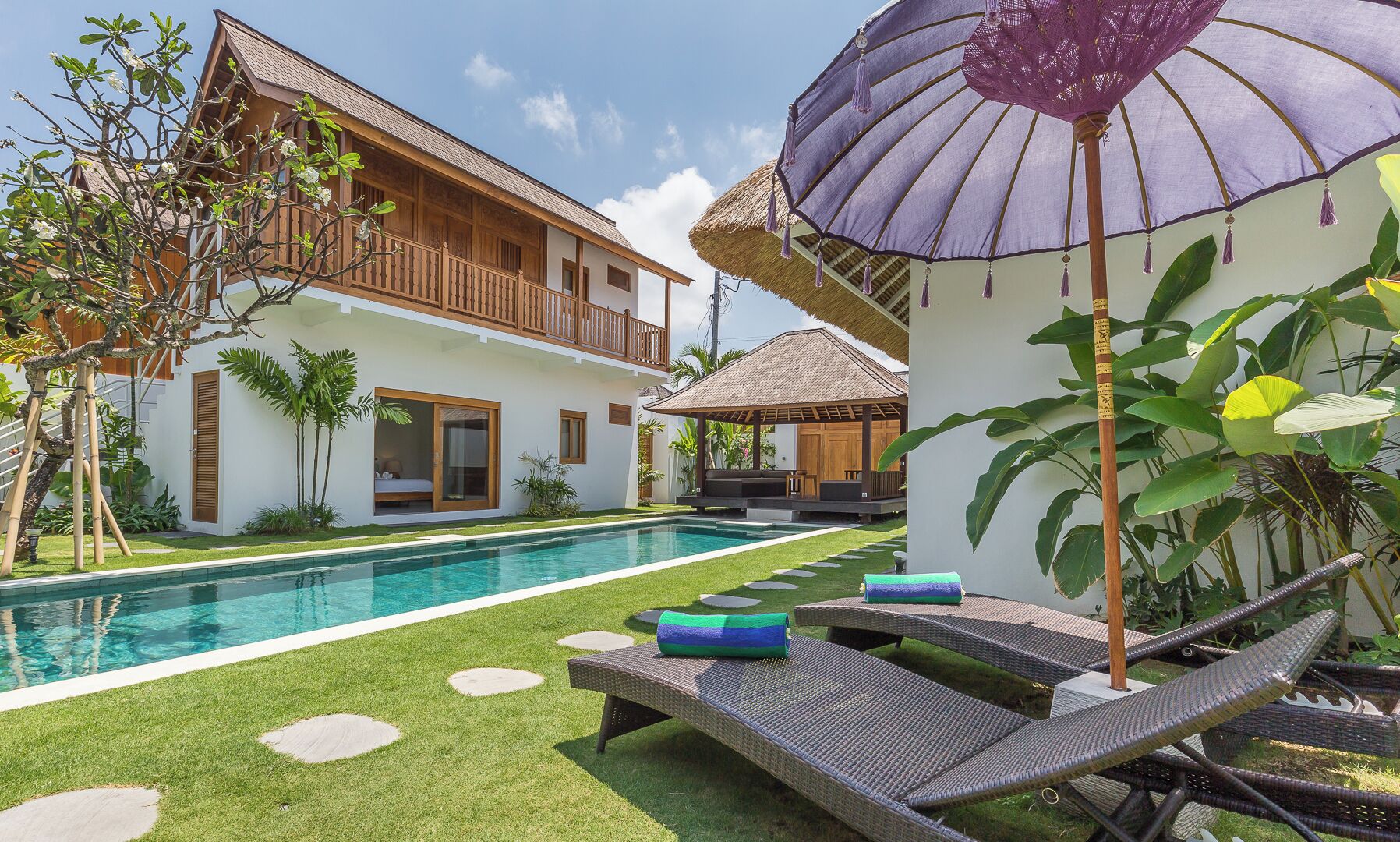 Une maison à deux étages avec une piscine, un espace salon extérieur et des plantes tropicales.