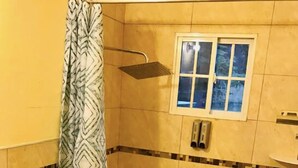 Ein Badezimmer mit Dusche, Toilette und einem kleinen Fenster über der Badewanne.