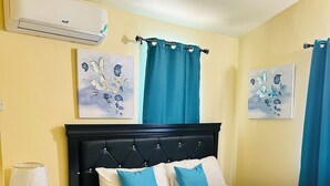 Ein Schlafzimmer mit einem Bett, einem Nachttisch, einer Lampe, einer Klimaanlage und zwei Wandbildern.