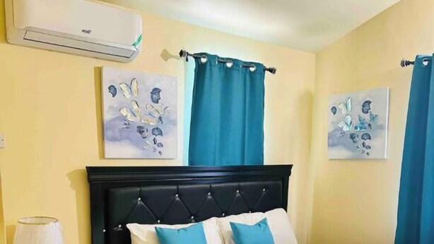 Ein Schlafzimmer mit einem Bett, einem Nachttisch, einer Klimaanlage und zwei Wandbildern.