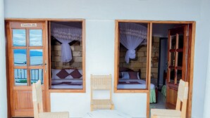 Una habitación con vista al mar a través de una ventana, una silla de madera, una mesa redonda pequeña y una cama también con vista.
