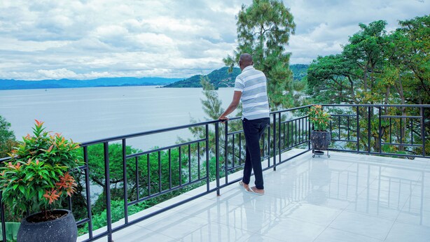 Un hombre de pie en un balcón con vista a un lago y montañas.