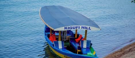Un bote con toldo que dice 'KIGUFI HILL' amarrado en una orilla arenosa.