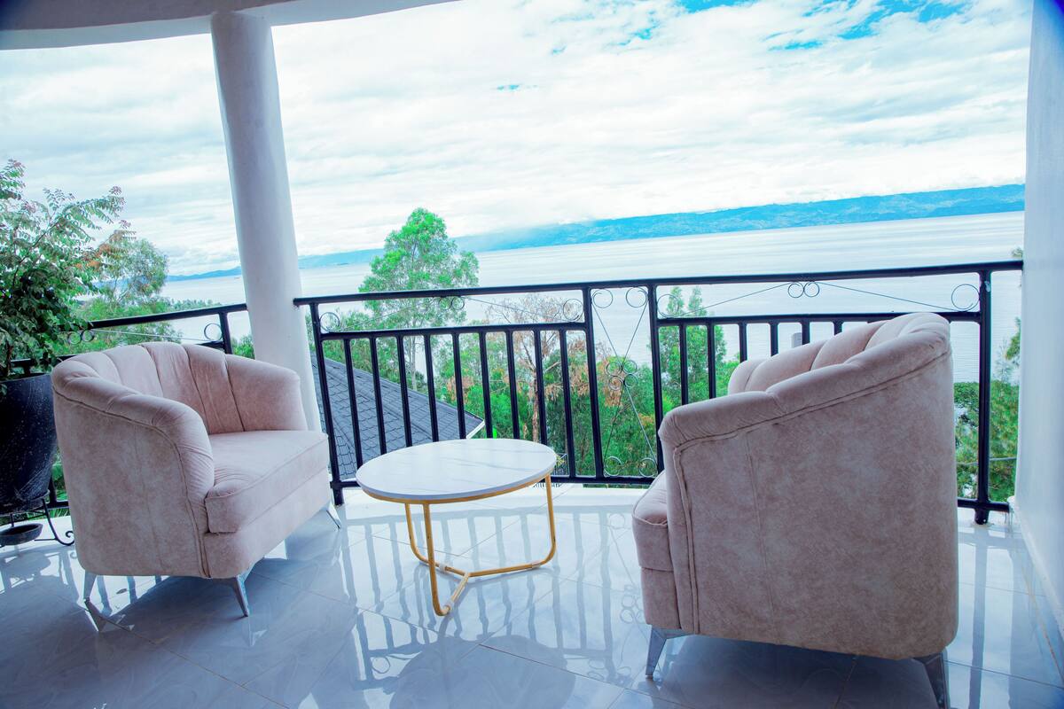 Ein Balkon mit zwei Sesseln und einem kleinen Tisch mit Blick auf ein Gewässer und viel Grün.