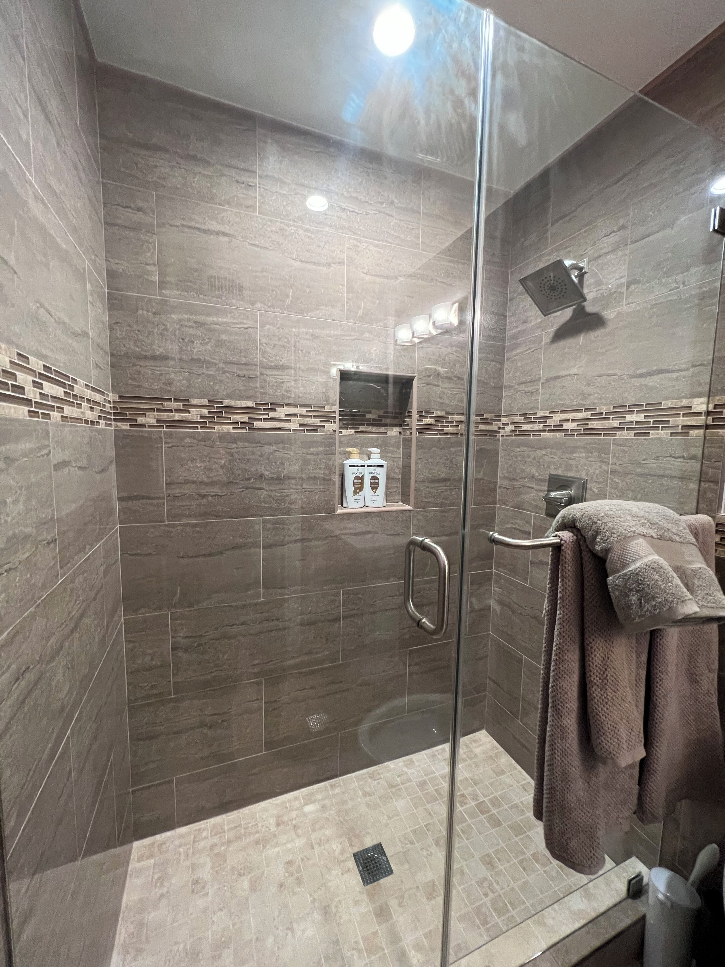 A modern shower area with a glass door, a handheld showerhead, and a towel rack.