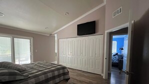 Een slaapkamer met een bed, een kledingkast, een televisie en een deur naar een andere kamer.