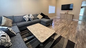 Een moderne woonkamer met een modulaire bank, een salontafel, een flatscreen televisie en een houten kast.