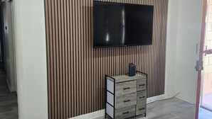 Una sala de estar moderna con un televisor de pantalla plana montado en una pared de listones de madera, un mueble de madera con cajones y un piso de madera gris.