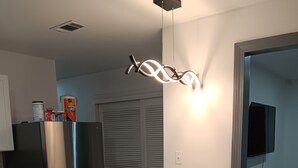 Una cocina moderna con un refrigerador de acero inoxidable, encimera de mármol, dos taburetes negros y una lámpara de techo original.