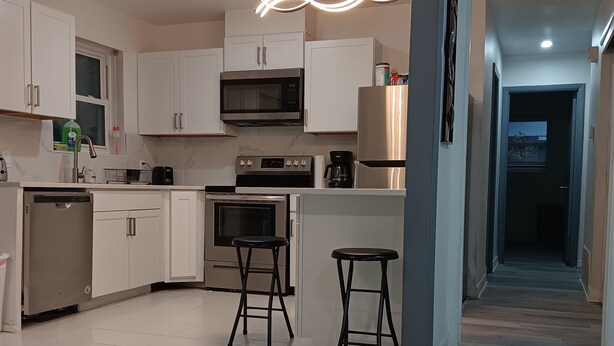 Una cocina moderna con armarios blancos, un microondas, estufa y dos taburetes.