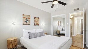 Une chambre à coucher comprenant un lit, des tables de chevet, un ventilateur de plafond et des œuvres d’art murales.