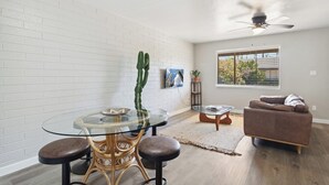 Un salon moderne avec une table à manger en verre, deux chaises en osier, un canapé en cuir marron, un cactus et un ventilateur de plafond.