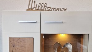 Um armário branco com uma placa de madeira que diz 'Welcome' em cima. No interior, há uma vitrine de vidro com um objeto em formato de coração.