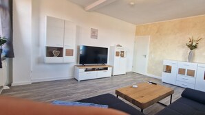 Uma sala de estar moderna com televisão de tela plana, armários brancos e uma mesa de centro de madeira.