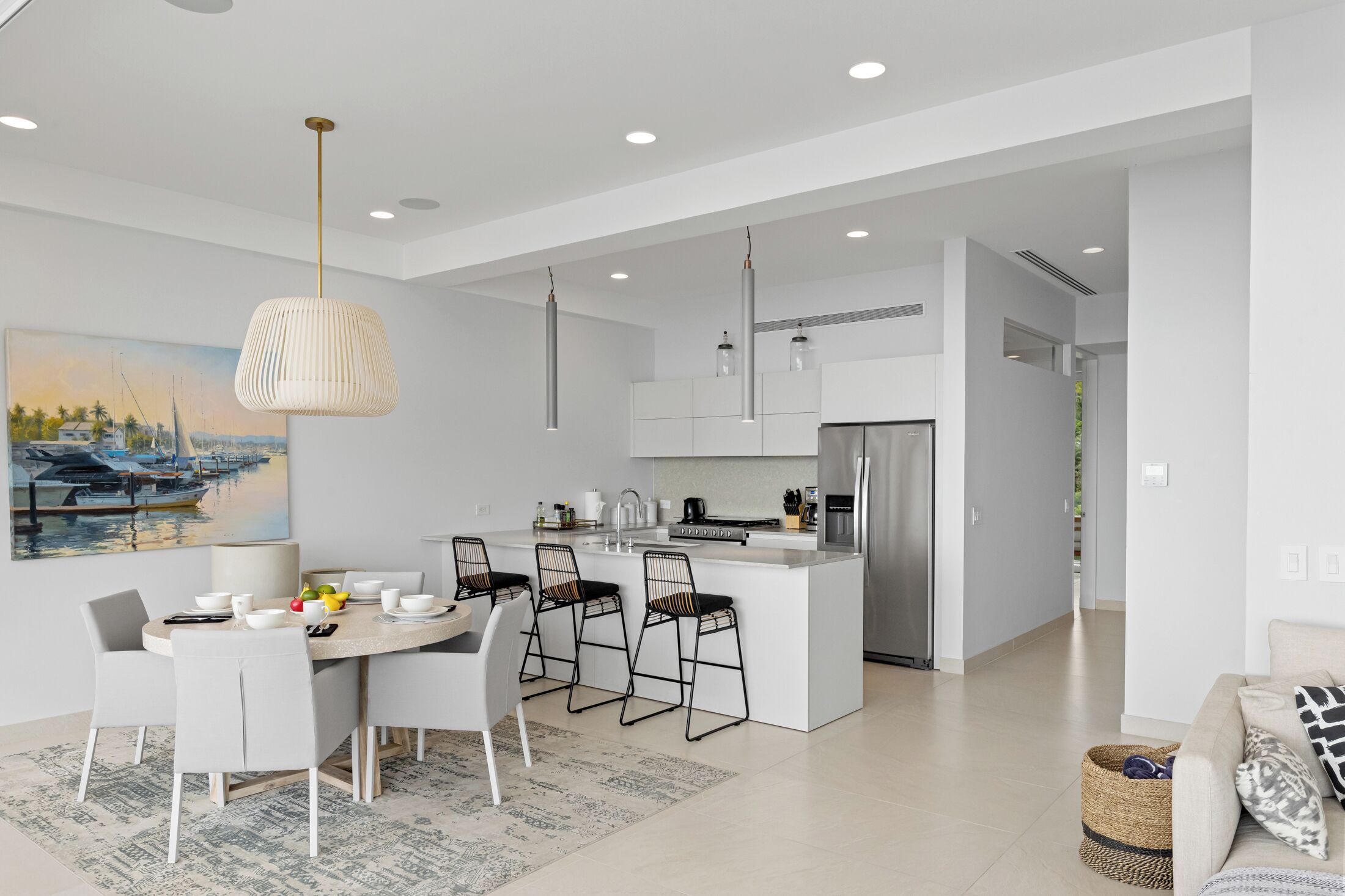 A modern kitchen with white cabinetry, a central island with bar stools, and a dining area with a white table and chairs.