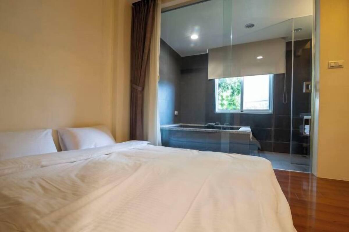 A hotel room with a bed, a glass shower enclosure, and a window.