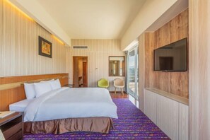 Une chambre d’hôtel avec un grand lit, un téléviseur fixé au mur et une vue sur l’extérieur, visible à travers une porte vitrée.