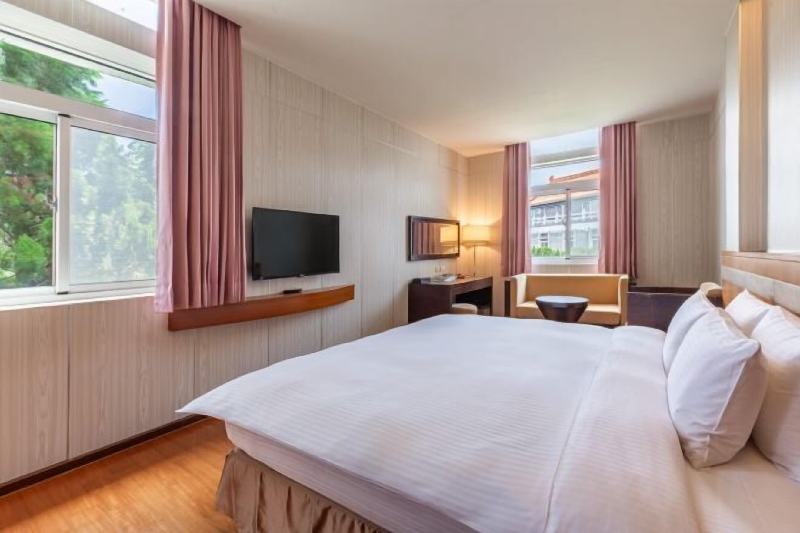 A hotel room with a large bed, a desk, a chair, a television, and a window with curtains.