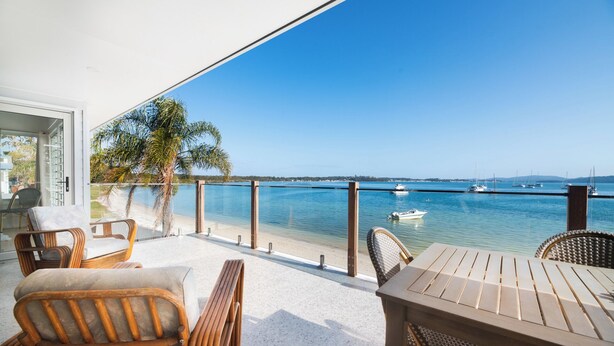 Un balcon agrémenté de meubles en osier, avec vue sur la mer et des bateaux à l’horizon.