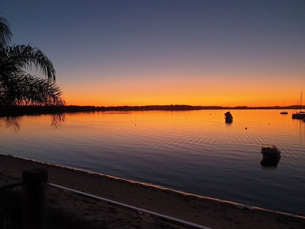 En stilla sjö vid solnedgången, med en båt i fjärran och en strand i förgrunden.